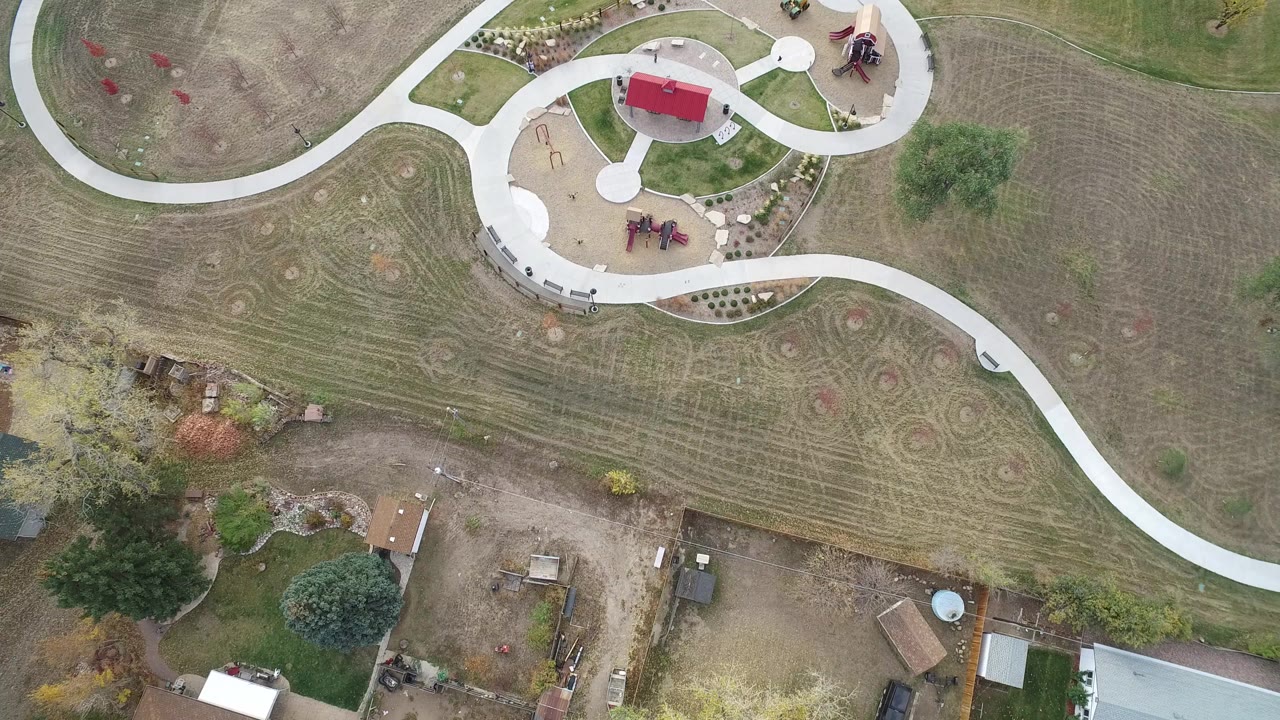 Opening overhead frame in Hidden Lake, Colorado showing curved concrete paths, a red-roofed play area, mowed grass, trees, and nearby residential yards with no visible people.
