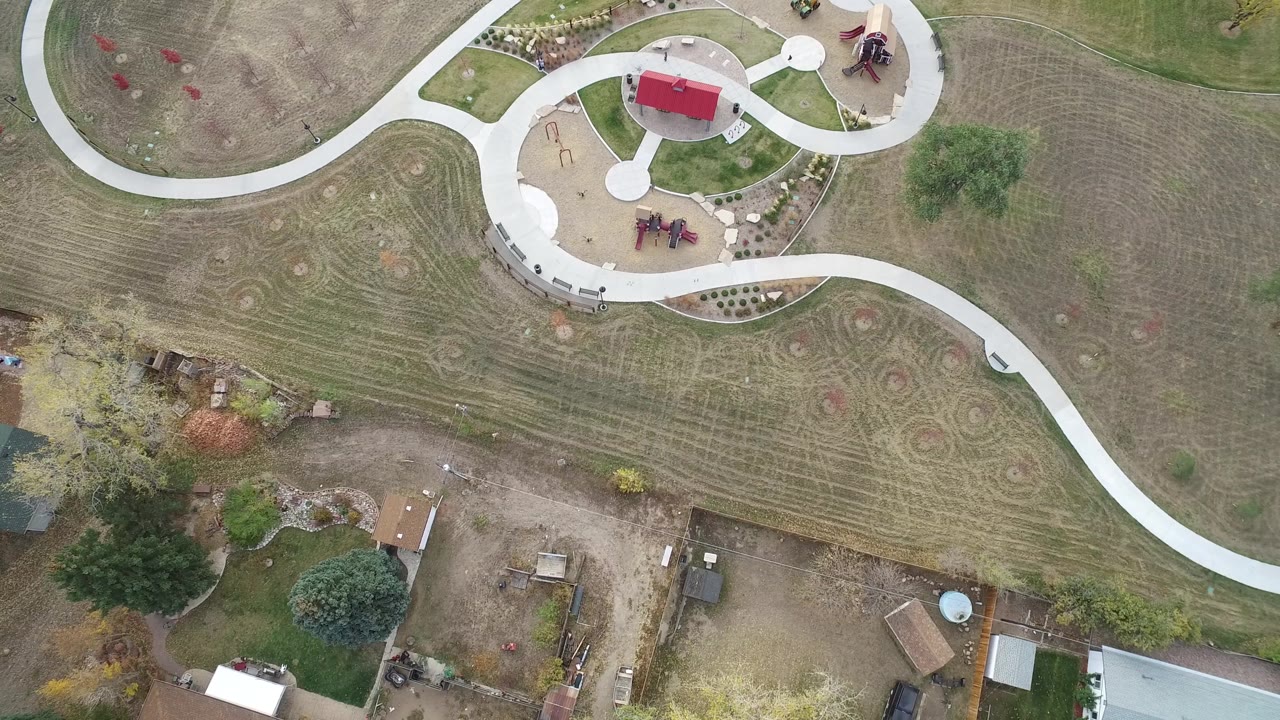Top-down drone view of park paths, mowed lawn patterns, and homes below.