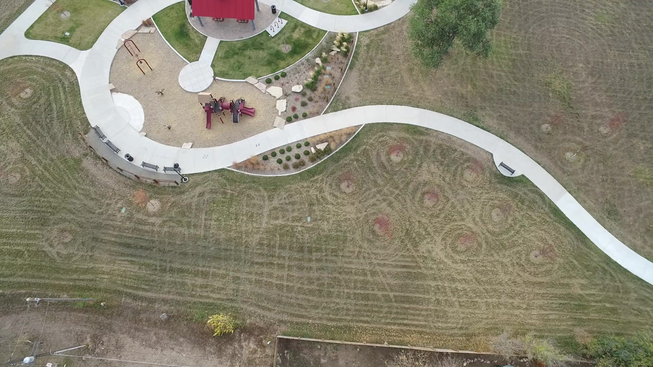 Overhead view of curving concrete paths, playground equipment, benches, and dry grass.