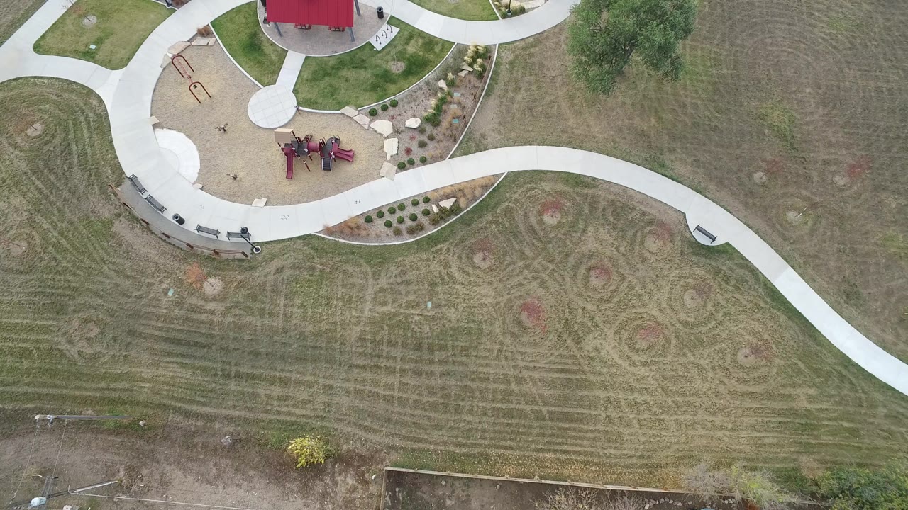 Aerial frame in Hidden Lake, Colorado with the winding concrete path running across the center, playground equipment near the top, landscaped beds, benches, and no visible people.