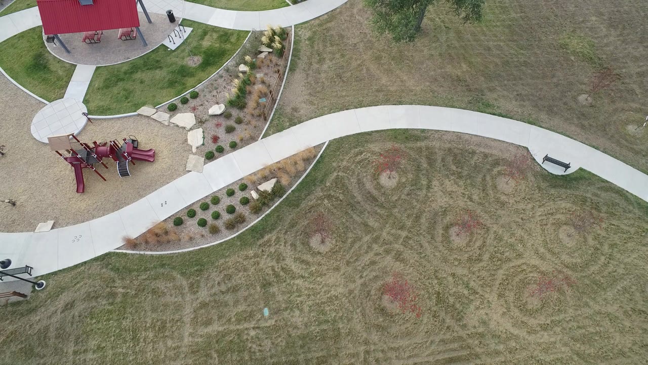 Top-down park view with red playground, shelter, paths, benches, and dry grass.