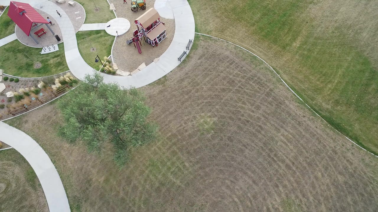 Overhead park lawn with curved paths and red-roof playground structures.