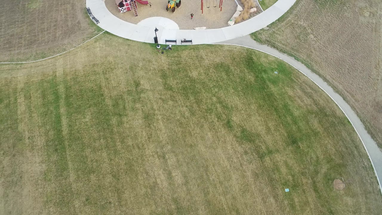High view of patchy grass with curved park path and playground.