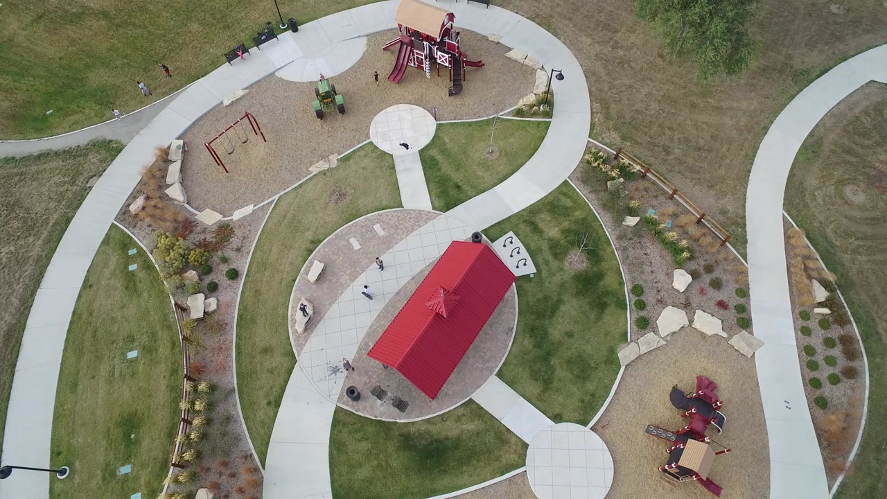 Overhead park view with red-roofed shelter, paths, playgrounds, and lawns.