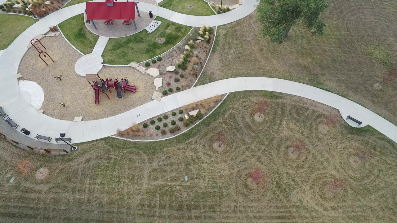 High overhead Hidden Lake, Colorado view with the red-roof pavilion near the upper edge, red playground structures below it, landscaped beds, grass, and no visible people.