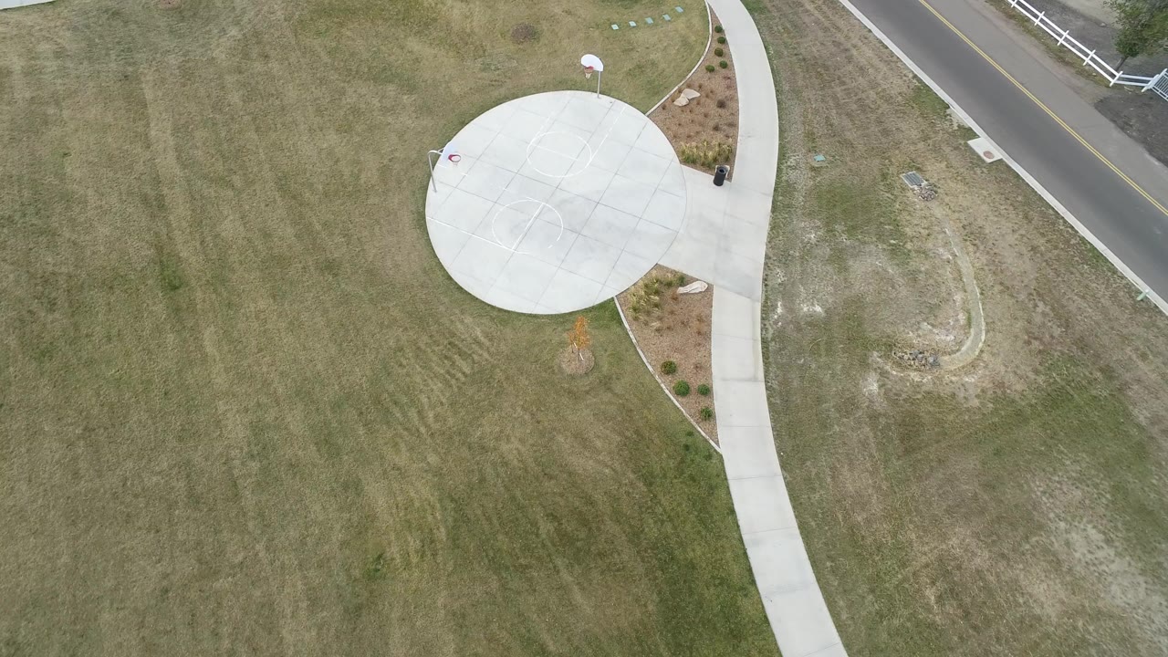 Overhead frame in Hidden Lake, Colorado showing a circular concrete pad connected to a curving walkway, surrounded by mowed grass and a road edge, with no visible people.