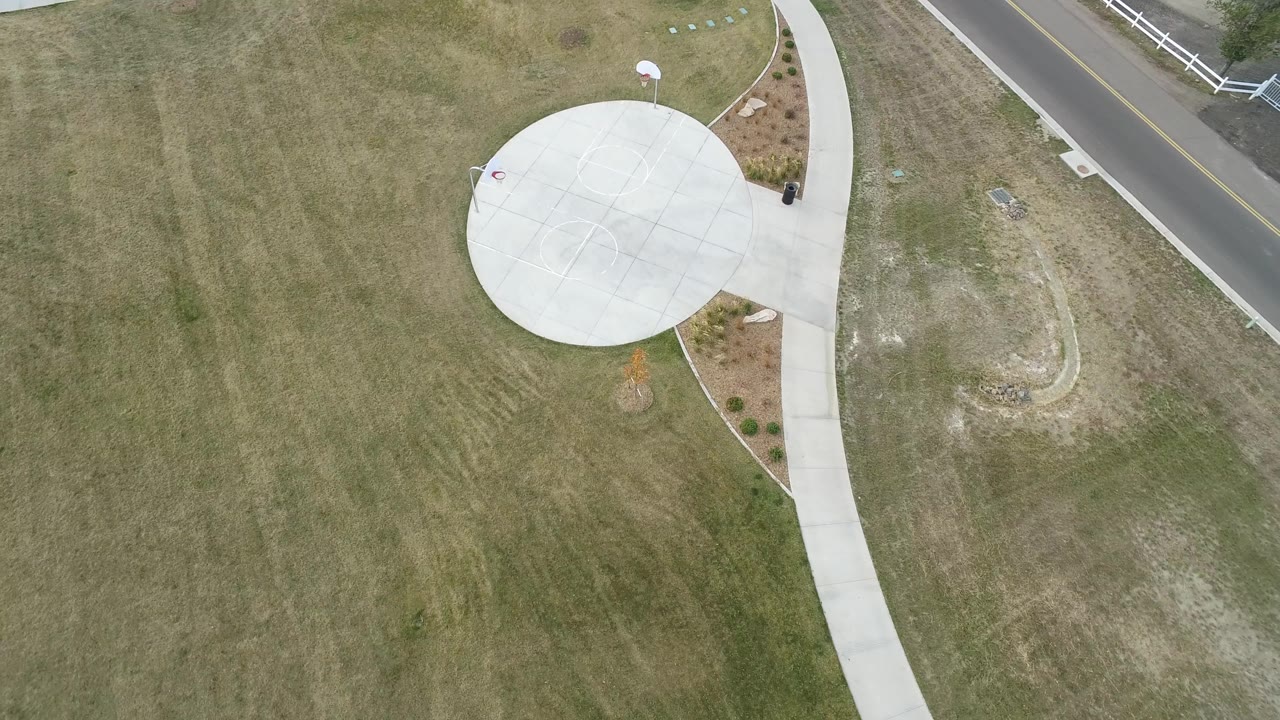 Aerial frame in Hidden Lake, Colorado with the round concrete area slightly higher in view, a pale sidewalk running downward, grass on both sides, and no visible people.