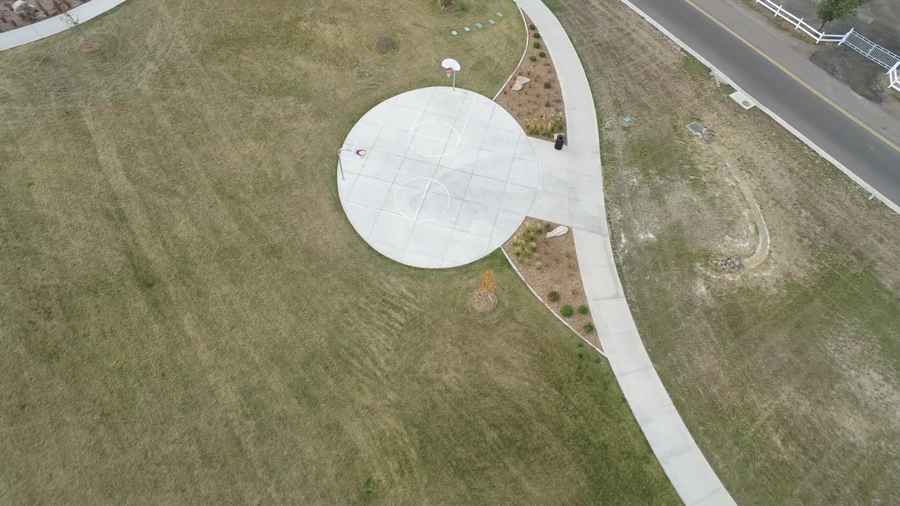 High-angle view of a round paved area and sidewalk beside open grass and a road.
