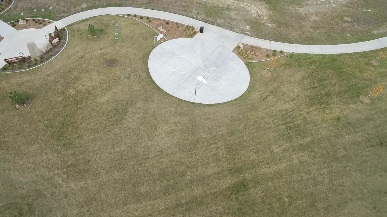 Overhead view of a circular basketball court beside curved paths and grass.