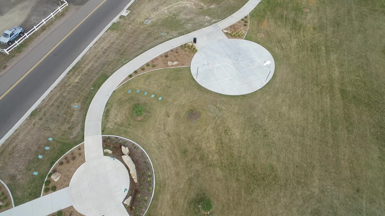 Top-down lawn view with road edge, white fence, curved walkway, and round concrete pad.
