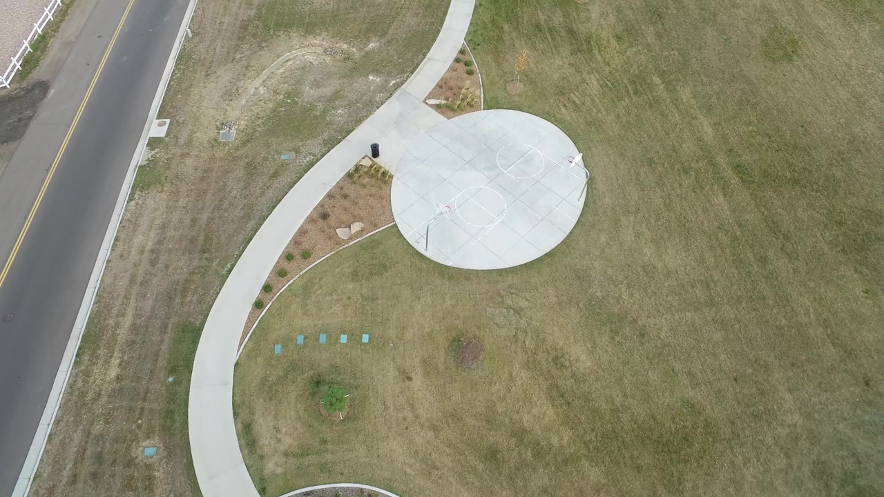 Hidden Lake, Colorado aerial view with the circular concrete pad near the upper right, the curved walkway crossing the grass, and the road running along the right side, with no visible people.