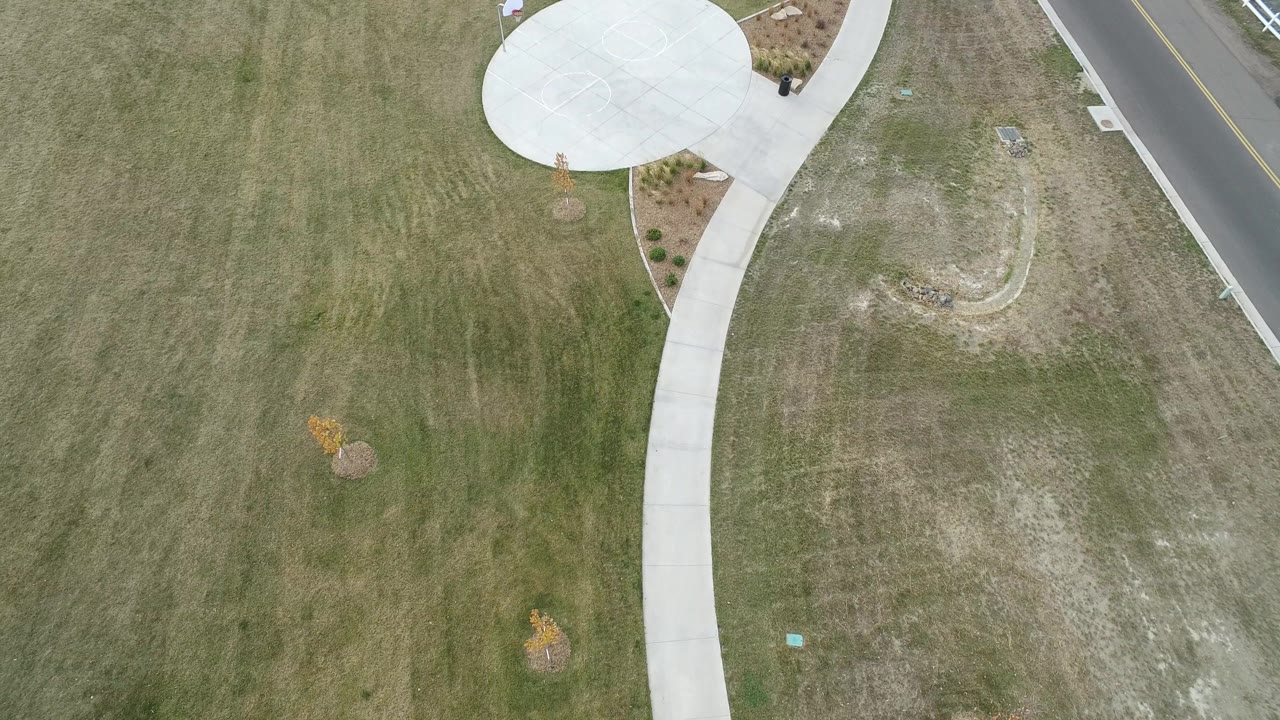 Hidden Lake, Colorado aerial frame with the open lawn dominating the view, the curved sidewalk running upward, the round concrete pad near the top edge, and no visible people.