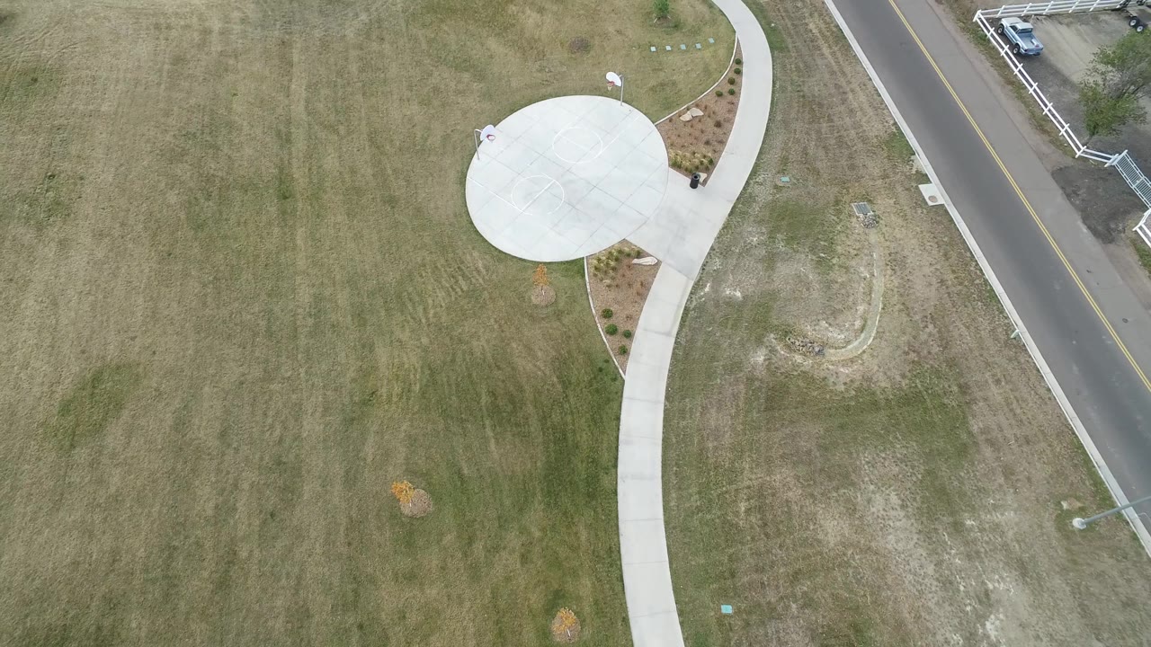 Aerial frame in Hidden Lake, Colorado with the circular concrete pad near the upper center, curving sidewalk below it, road along the right side, and no visible people.