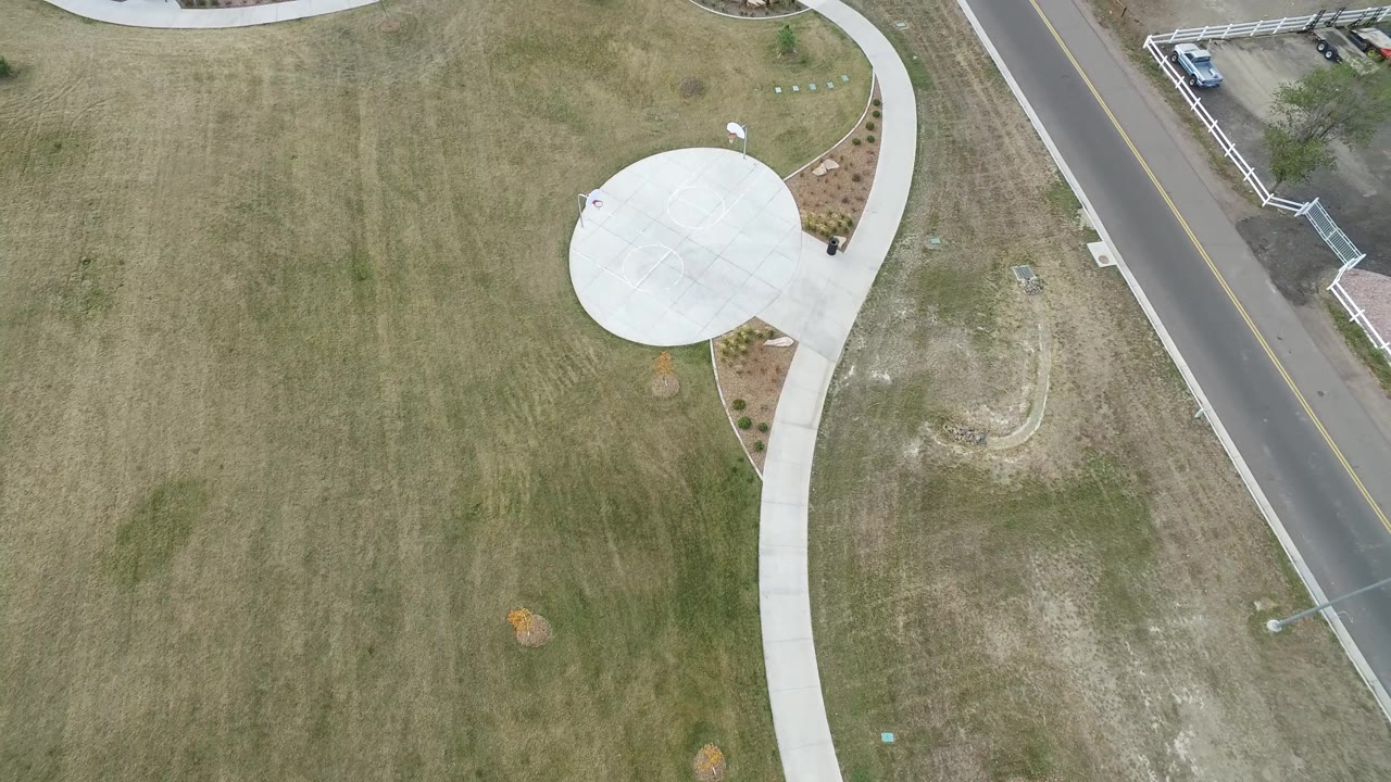 High drone view in Hidden Lake, Colorado showing the sidewalk loop shifted slightly across the grass, with the road and curb at right and no visible people.