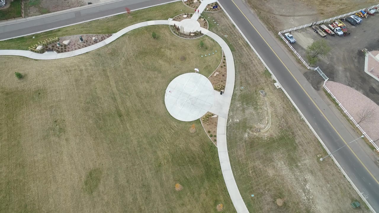 A second overhead moment in Hidden Lake, Colorado shows the circular concrete area shifted right, a long curved walkway across the grass, parked cars near the upper road, and no visible people.