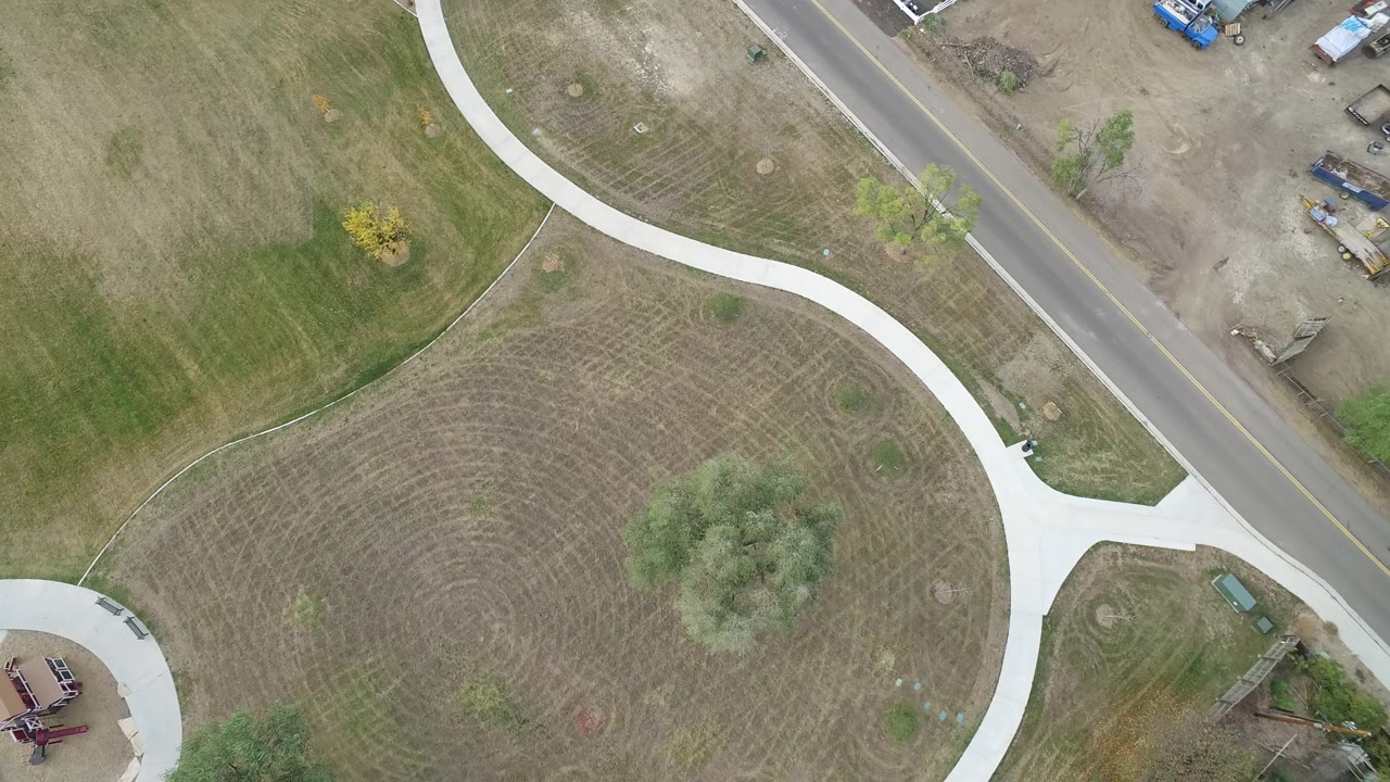 Top-down view of a circular grass area crossed by a white path beside a road.