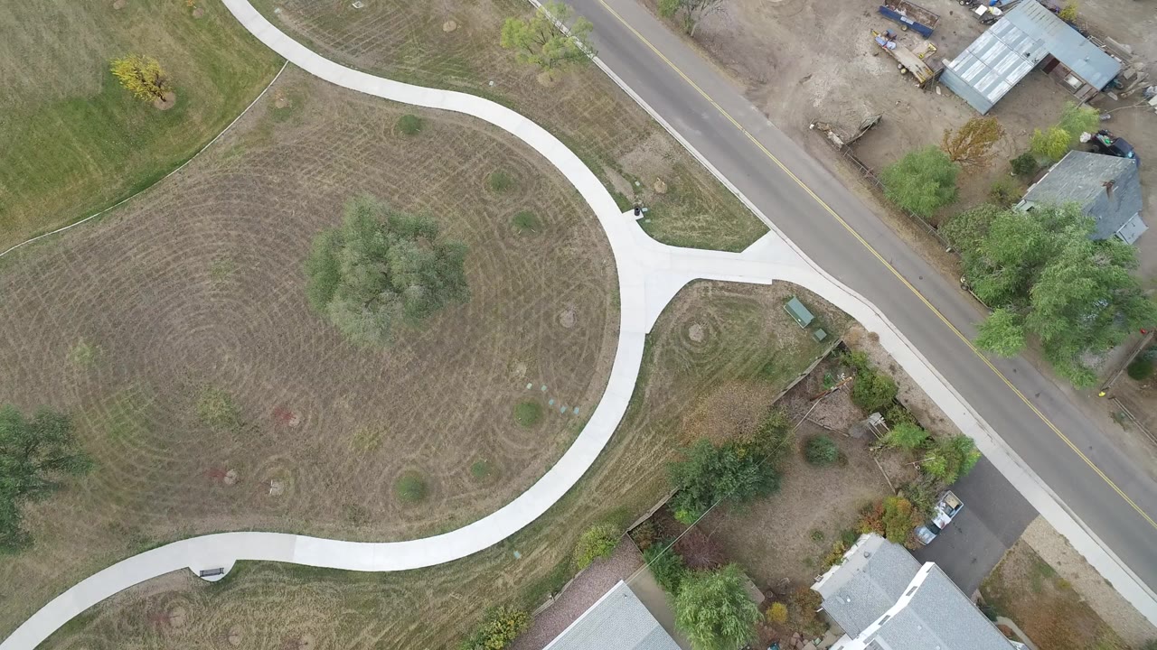 Overhead view of curved concrete path, road, trees, yards, and small buildings.