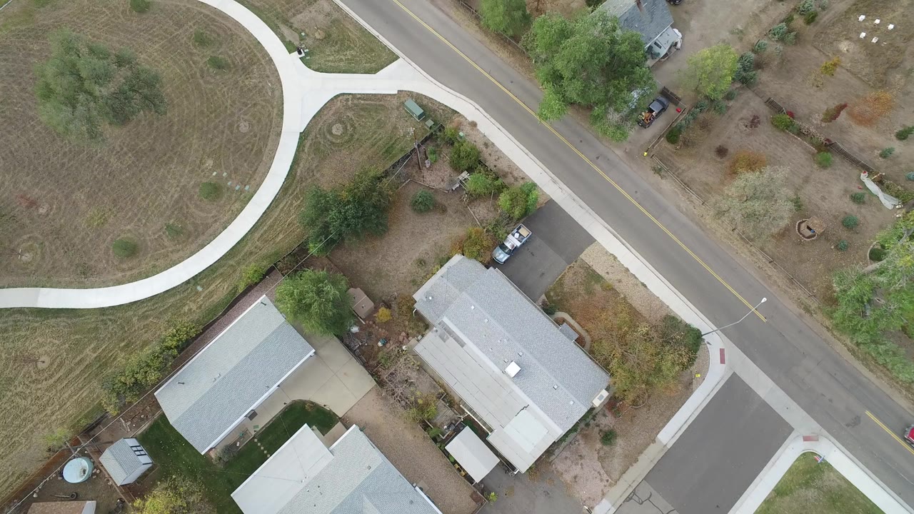 Overhead view of rooftops, road, sidewalks, lawns, and trees.