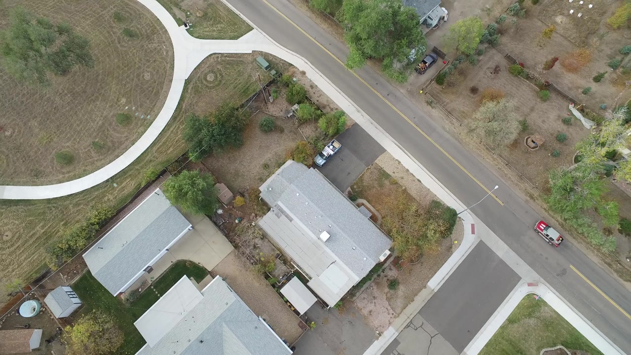 Overhead Hidden Lake, Colorado frame showing a red vehicle on the road, several parked vehicles near driveways, pale roofs, sidewalks, yards, and no visible people.