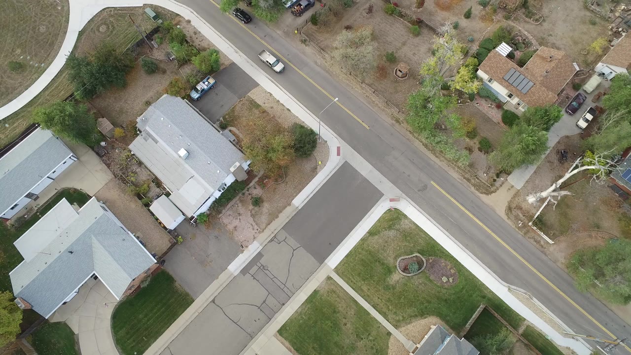 Overhead view of a residential road with homes, yards, sidewalks, and a light-colored car.