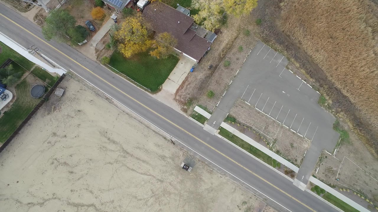 Hidden Lake, Colorado aerial frame with the road cutting diagonally past lawns, houses, dry open ground, and a mostly empty parking lot, with no visible people.