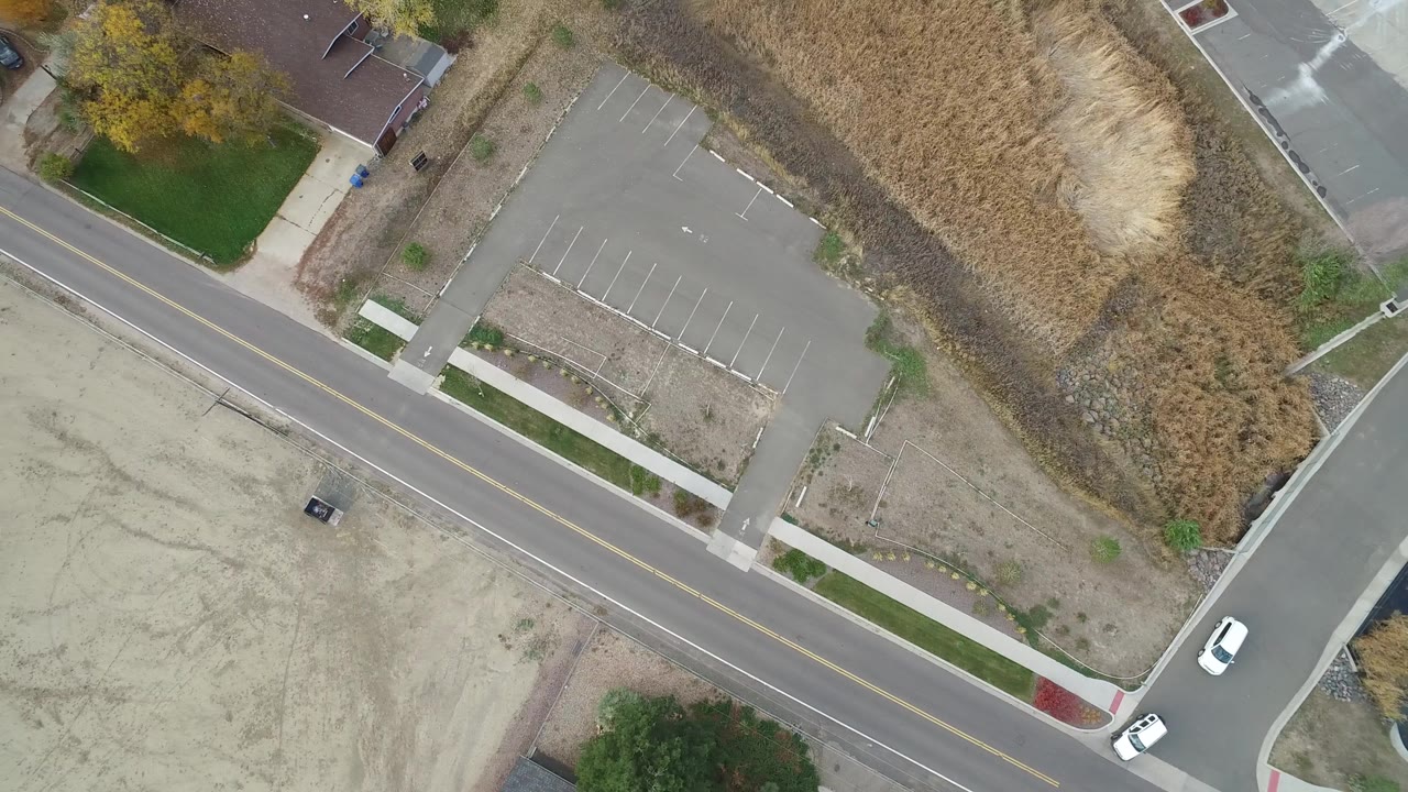 Overhead frame in Hidden Lake, Colorado showing a diagonal avenue, empty marked parking lot, dry grassland, sidewalks, a small building edge, and no visible people.