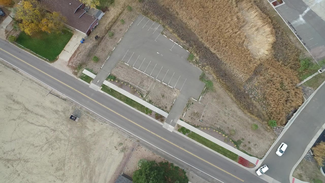 Hidden Lake, Colorado aerial frame with a white car near a side-road corner, an empty parking lot, sidewalks, dry grass, and no visible people.