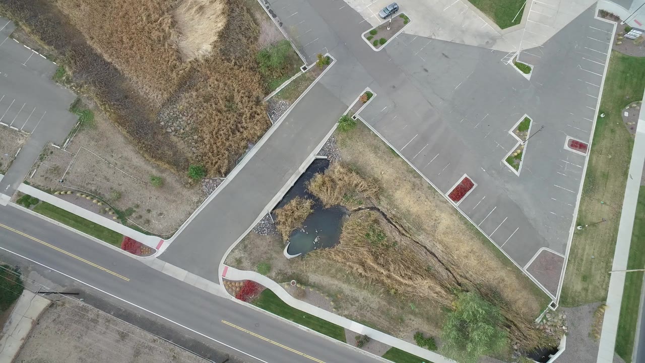 Overhead view of roads, parking lot, dry grass, and a small pond.