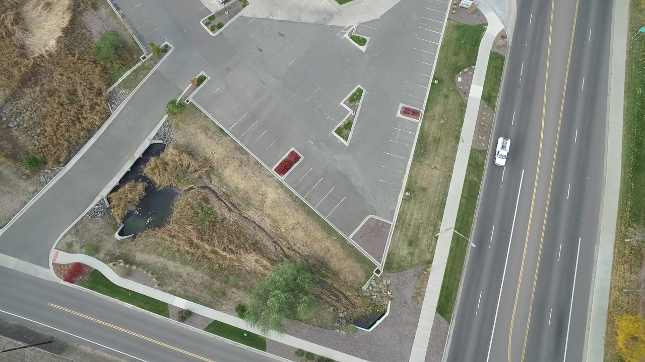 Overhead road, parking lot, sidewalk, dry grass, and small water feature.