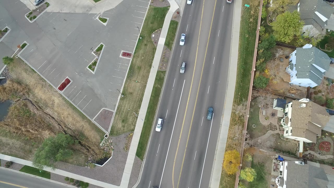 Overhead view of a multi-lane road beside a parking lot and houses.
