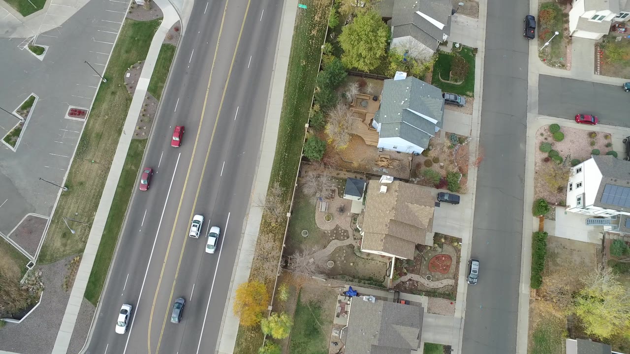 Hidden Lake, Colorado aerial frame with white and dark cars traveling along the road, landscaped residential yards, roofs, driveways, parked cars, and no visible people.