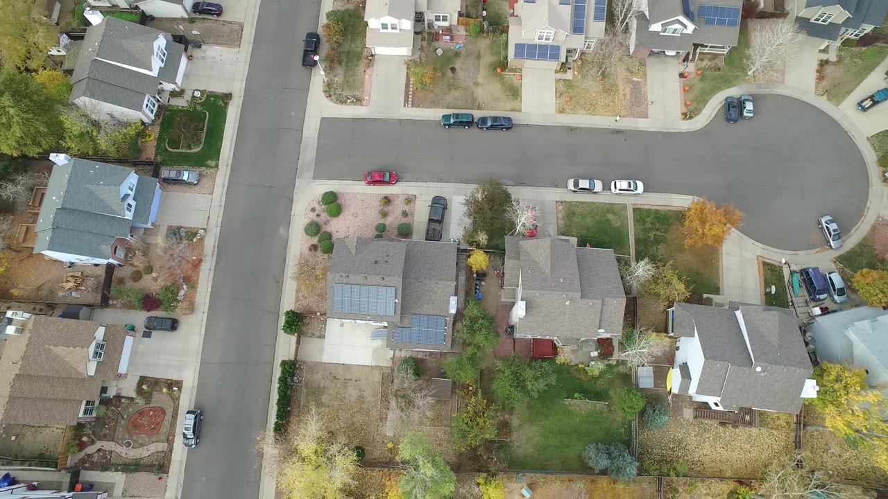 Aerial overhead view in Hidden Lake, Colorado showing the cul-de-sac center, adjacent road, rooftops, parked cars, patchy lawns, and no visible people.