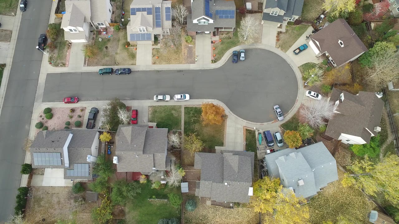 Overhead residential street with houses, driveways, parked cars, and trees.