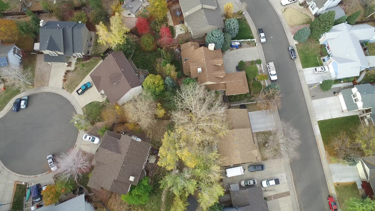 Overhead view of a cul-de-sac with houses, driveways, parked cars, and trees.