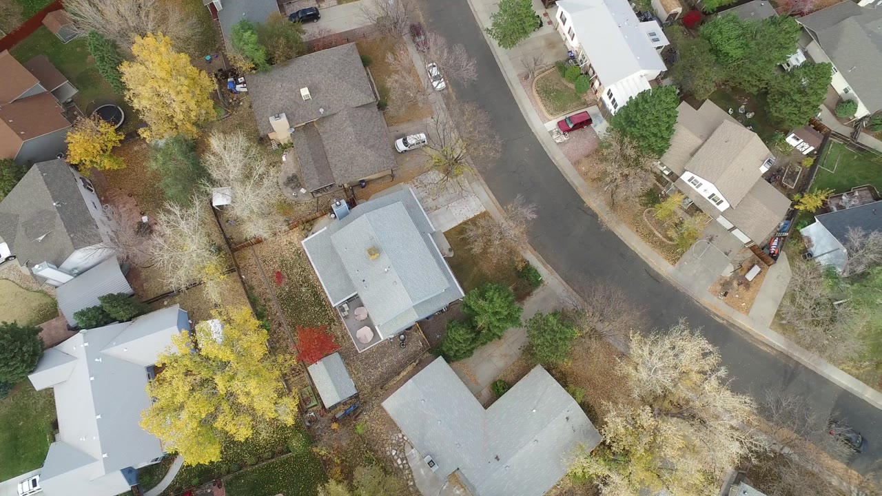 Aerial view over Hidden Lake, Colorado with a gray-roofed home near center, a curved street at the top, pale driveways, parked cars, mixed trees, and no visible people.