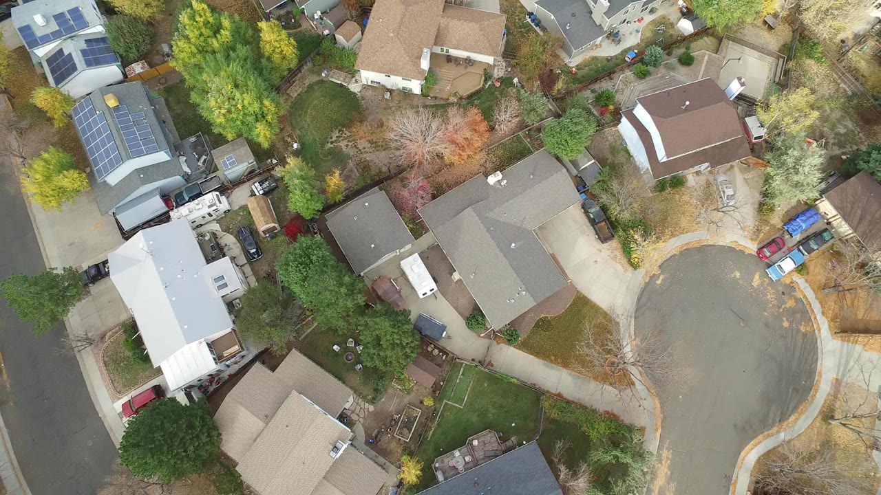 Overhead residential cul-de-sac with houses, trees, and parked vehicles.
