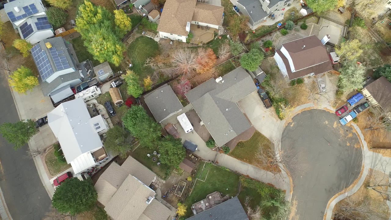 Drone-height overhead frame in Hidden Lake, Colorado with rooftops, a rounded street end, fenced yards, mature trees, and no visible people.