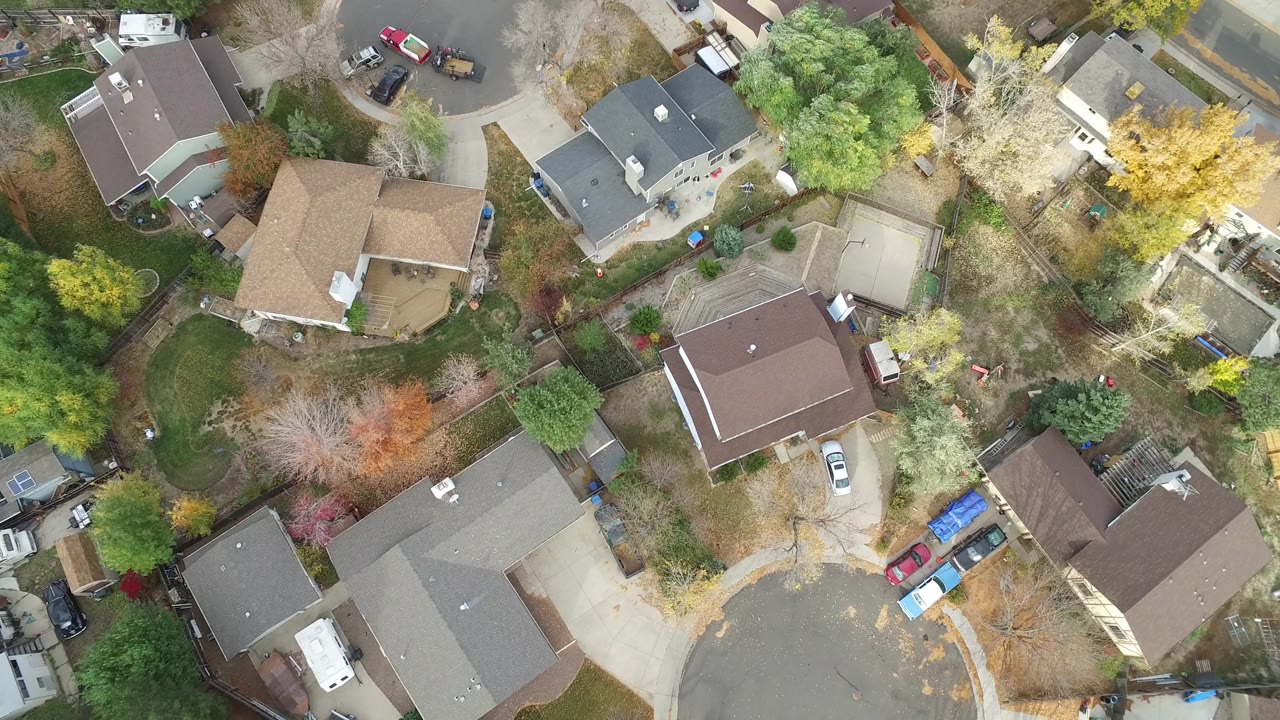 Overhead suburban houses, yards, streets, trees, and parked cars.