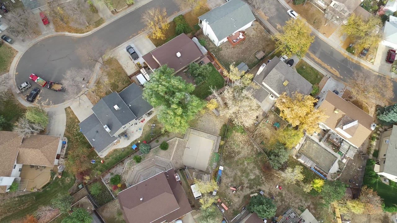 A high overhead frame of Hidden Lake, Colorado showing detached homes, a curved residential street, autumn trees, driveways, and parked cars, with no visible people.
