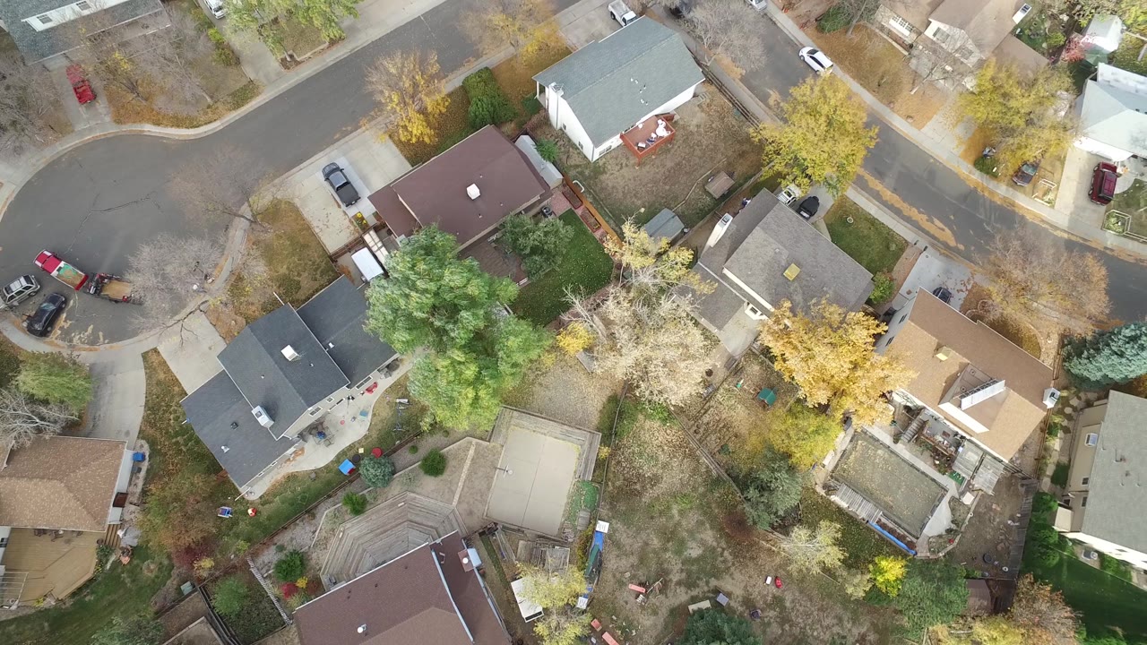 Aerial view of houses, lawns, autumn trees, and a residential curve.