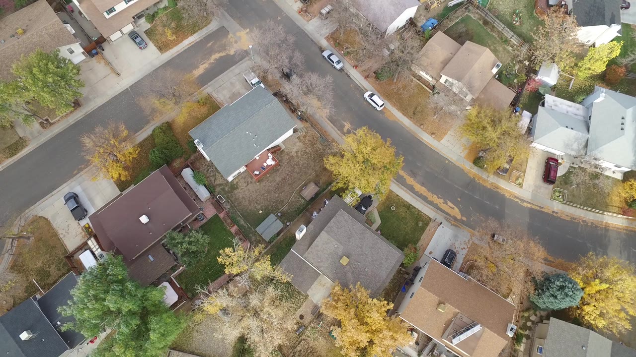 Straight-down aerial view over Hidden Lake, Colorado homes, driveways, parked cars, fenced yards, and autumn trees at the opening moment, with no visible people.