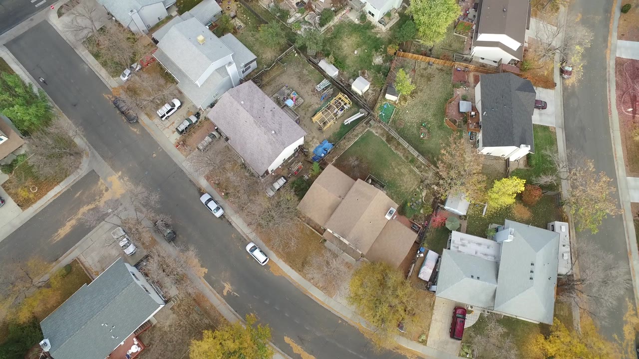 Aerial view of residential blocks with parked cars, sidewalks, and fenced yards.