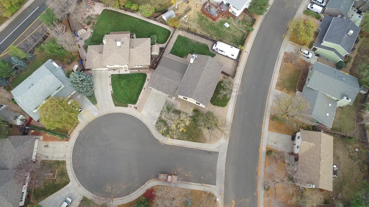 Top-down Hidden Lake residential view with tan and gray rooftops, the rounded end of a street, clipped green yards, driveways, parked vehicles, and scattered trees.