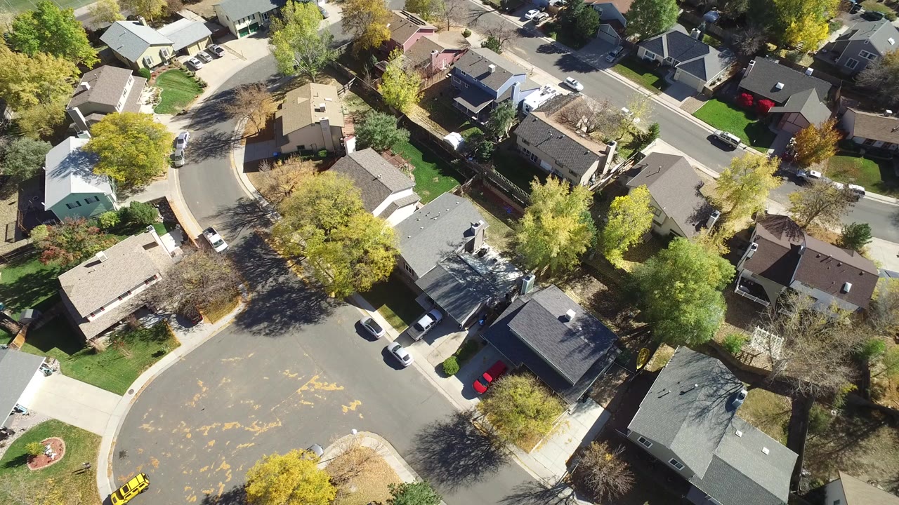 Overhead view of houses, streets, lawns, cars, and trees.
