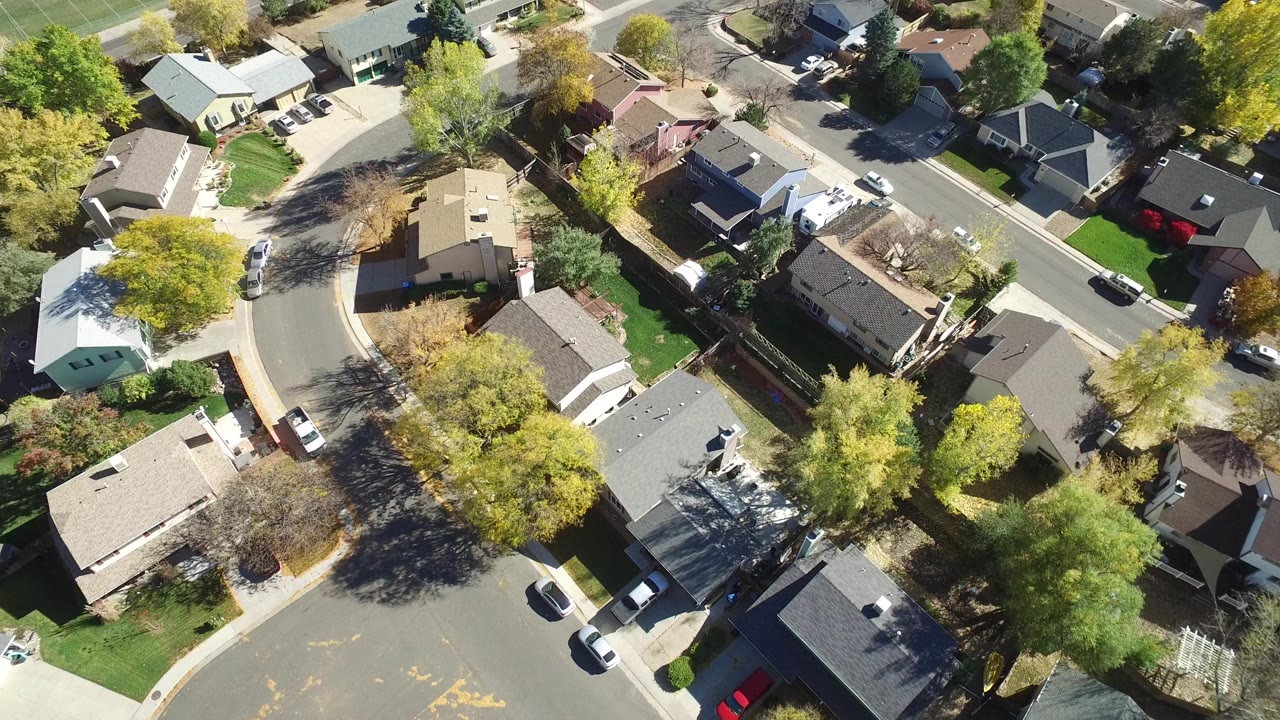 Aerial view of suburban houses, curved street, trees, and parked cars.