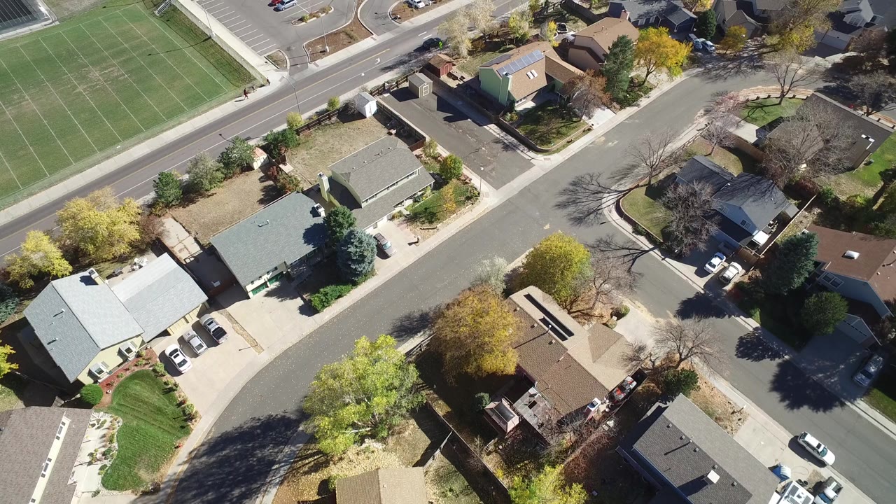 A later aerial angle over Hidden Lake, Colorado, keeps the green sports field near the top while rooftops, parked cars, and sunlit trees fill the center, with no visible people.