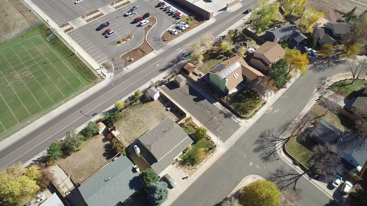 Aerial view of houses, a road, a green sports field, and a parking lot.