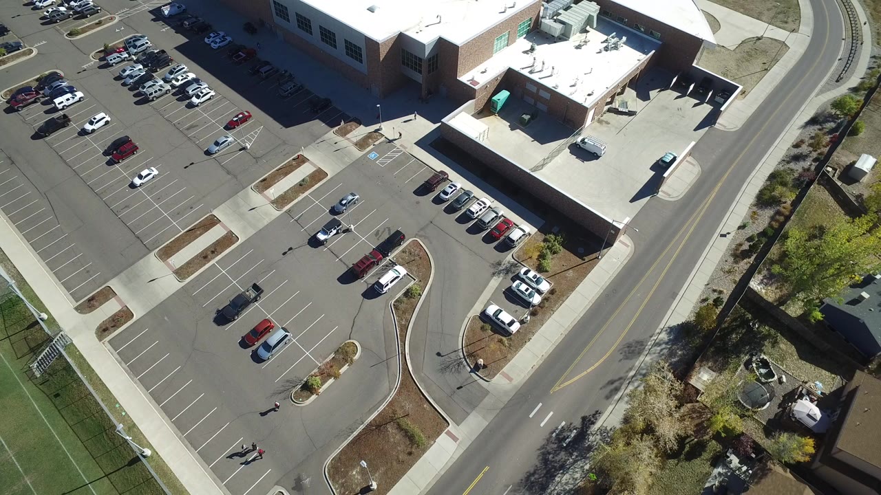 High aerial frame over Hidden Lake, Colorado showing marked parking spaces, scattered cars, a large flat-roofed building, a curved road, sidewalks, and no visible people.