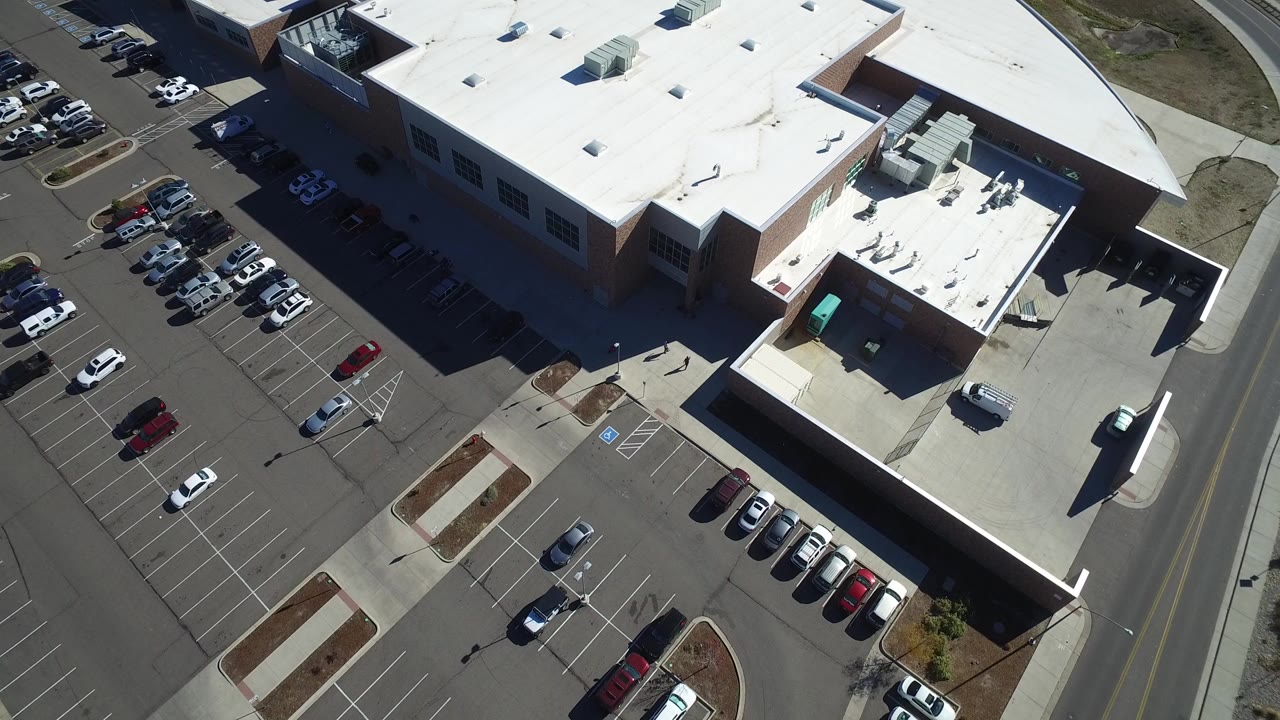 Aerial view of a large white-roofed building beside a parking lot.