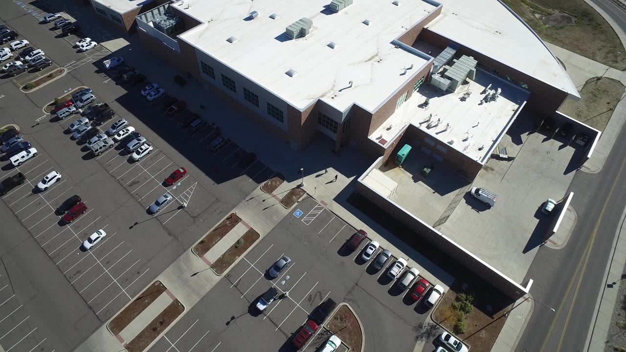 Aerial view in Hidden Lake, Colorado centered on the white roof and rooftop equipment, with parking spaces and cars along the left side and no visible people.